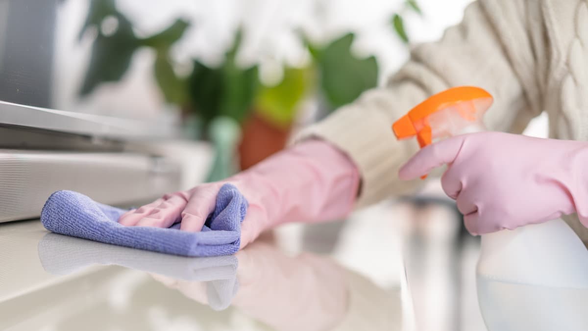 House cleaning in Greater Seattle: gloved hand wiping a tabletop with a microfiber cloth and spray.