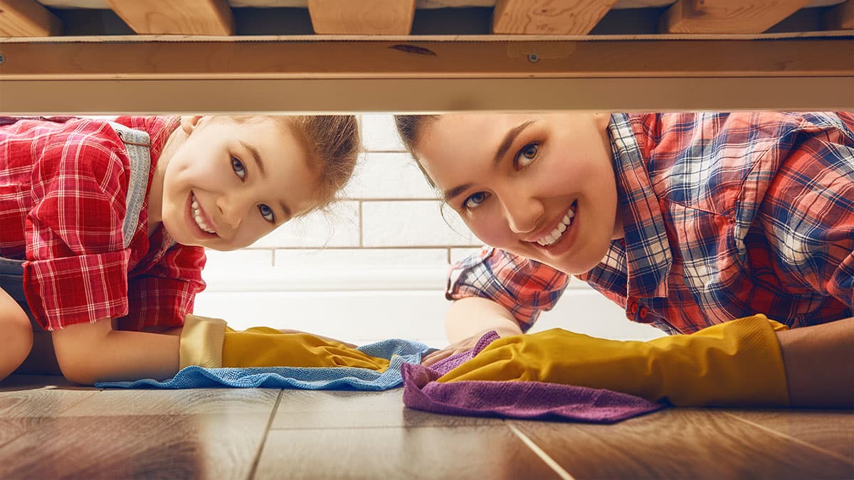Mother and child dusting under furniture during a weekly cleaning routine for a busy Redmond WA household.