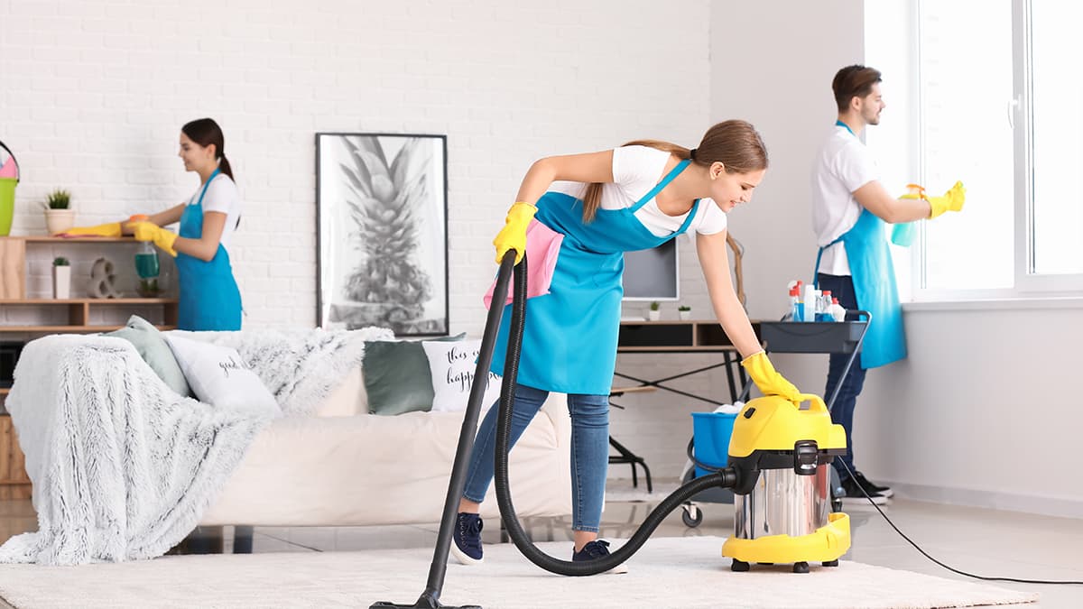 Team vacuuming a living room rug and cleaning windows and shelves, illustrating deep cleaning services for Medina homes.