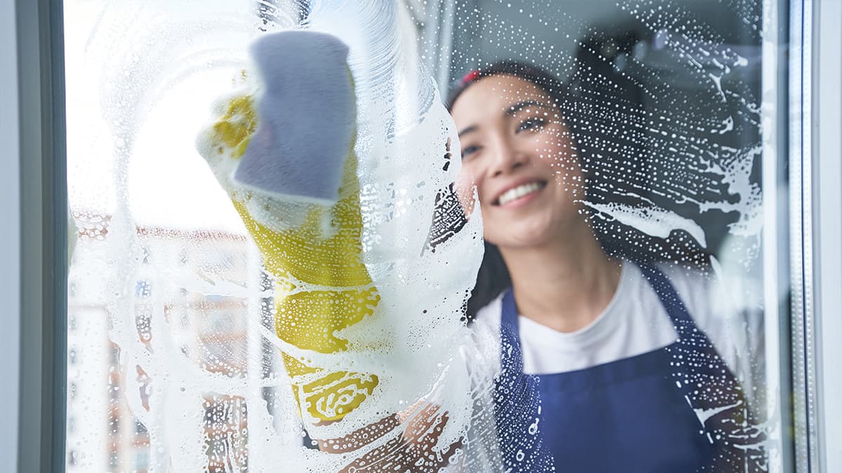 Cleaner washing a soapy window with a cleaning pad and yellow protective gloves.
